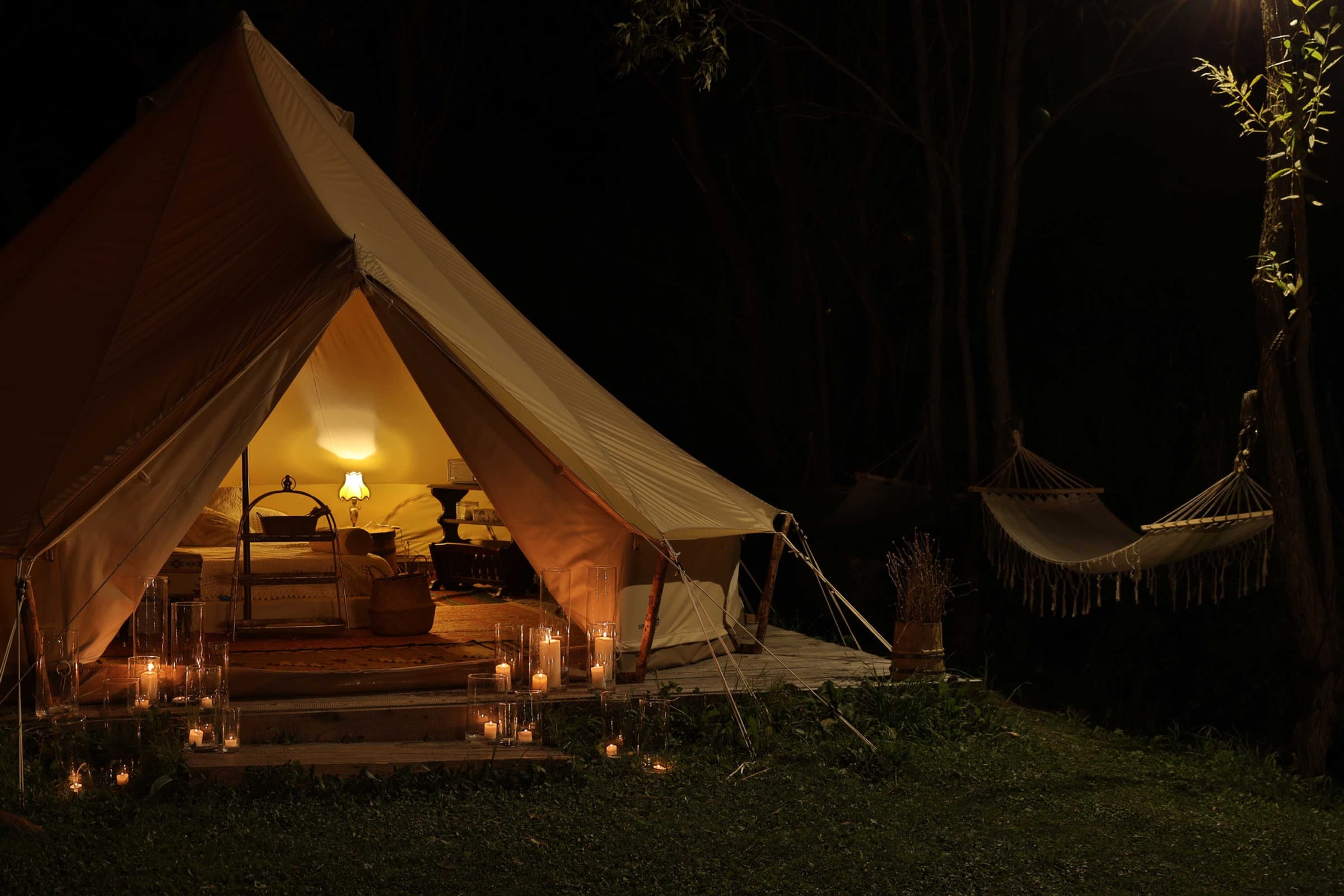 Beleuchtetes Glamping-Zelt mit Kerzen und Hängematte bei Nacht